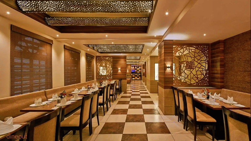 Restaurant interior with long rows of tables, chairs, checkered flooring, and ceiling lights.