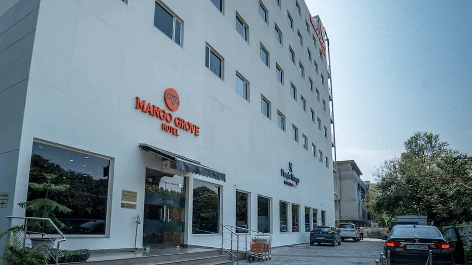 Daytime exterior view of the hotel building with signage and parking at Mango Grove Hotel.