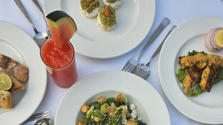 Multiple plates of neatly arranged food placed alongside cutlery and fresh juice on a clothed table at A.S. Hotels, Khajuraho.