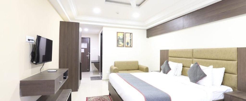 Full view shot of a brightly lit Premium Room at Pravasa Ahmedabad featuring a double bed and a wall mounted television placed opposite to it.