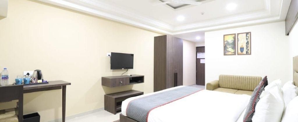 Full-view shot of the Premium Room at Pravasa Stay, Ahmedabad (Alba Premier), featuring a comfortable double bed along with a work desk and a wall-mounted television in front of it.