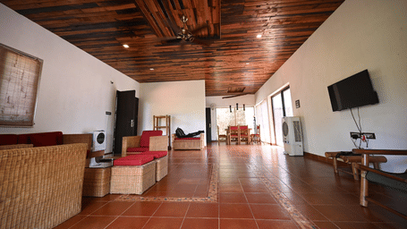 A long room with a wooden floor, tan furniture, and a television on the wall.