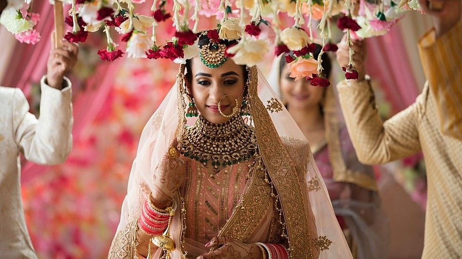 Indian bride walking down the aisle with four brother around her. The brother are holding a decorated small flower blanket above her head.
