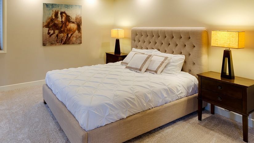 A bedroom with warm interiors, a neatly made bed, a bedside table with a table lamp, and a photo frame on the wall - Hotel Lalita Grand