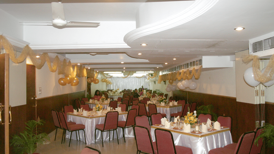 An decorated indoor event hall arranged with round dining tables draped in white tablecloths and surrounded by chairs.