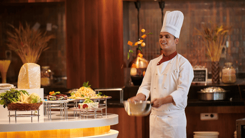 A chef bringing food to the buffet spread.