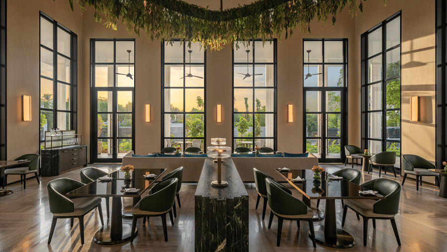 Eden bar seating with green leather chairs, black marble tables, a hanging greenery installation and tall black-framed windows at The Residency Signature Madurai.