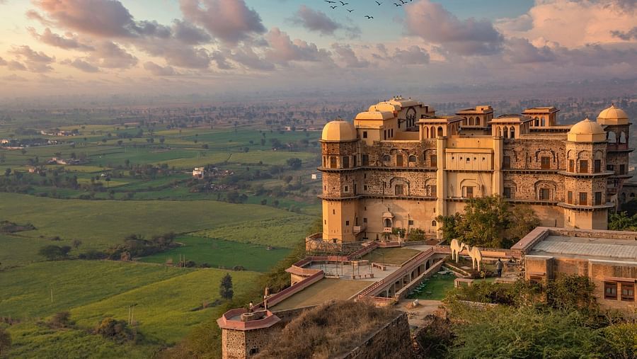 Face view of Rani Mahal perched on a hill at Tijara Fort-Palace - 19th Century, Alwar with green landscape and colourful sky in the background.