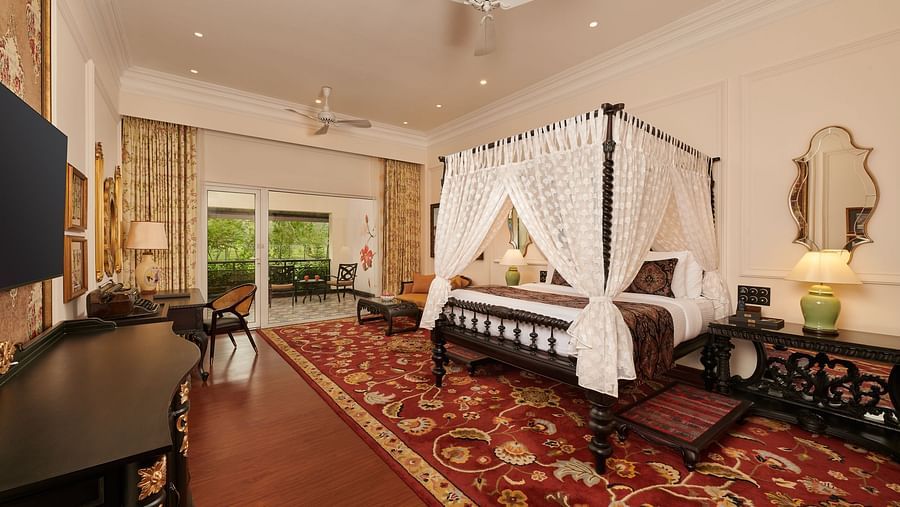 Four-poster bed in a spacious suite with vintage decor and carpeted flooring.