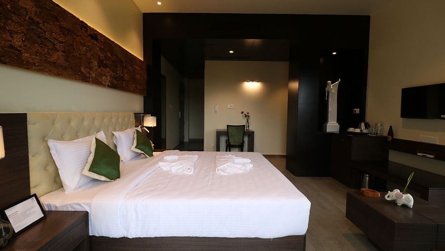 A hotel bedroom with a large, white-linened bed, bedside tables with lamps, and a glimpse of a television, featuring wooden wall panelling - Sea Hills Hotels, Sri Vijaya Puram (Port Blair)
