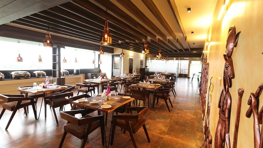 A wide view of a spacious restaurant with numerous wooden tables and chairs, warm lighting, and decorative wall panels and statues, giving an inviting ambiance - Sea Hills Hotels, Sri Vijaya Puram (Port Blair)