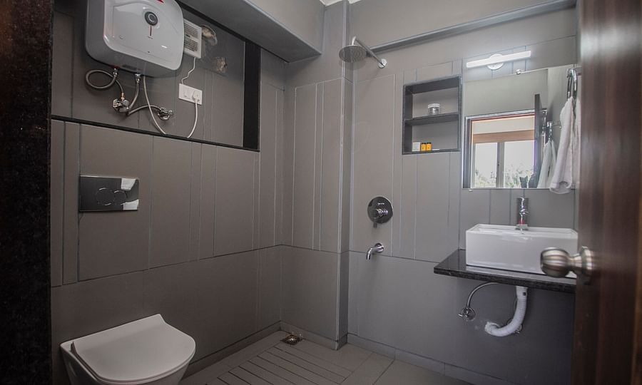 Modern bathroom with a wall-mounted toilet, overhead shower, sink with vanity mirror, water heater, and minimal grey-toned décor - Central Heritage Resort and Spa