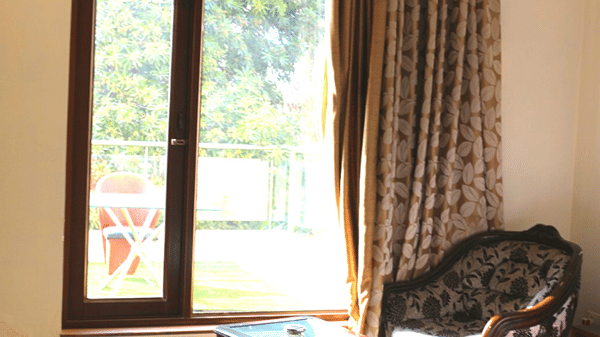 Sunlit guest room corner with a large window, cosy seating and elegant curtains.