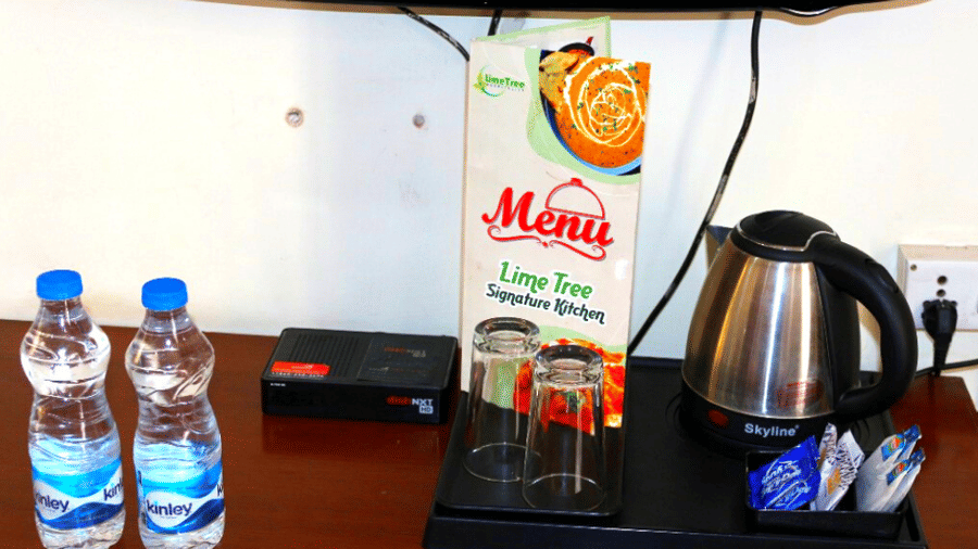 In-room amenities including a wall-mounted TV, dining menu, electric kettle, two water bottles, and glasses on a tray.
