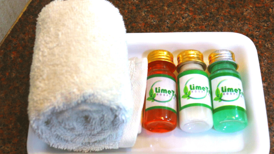 Bath amenities showing rolled white towels and three branded toiletry bottles arranged neatly on a wooden tray.