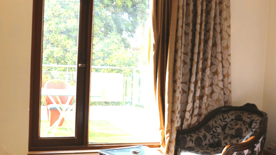 Sunlit guest room corner with a large window, cosy seating, elegant curtains and peaceful outdoor views creating a relaxing ambience.