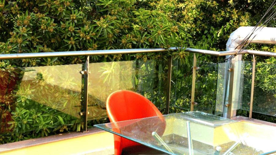 Terrace seating with a glass-top table, a red chair, a glass balustrade, and potted greenery overlooking the surroundings.
