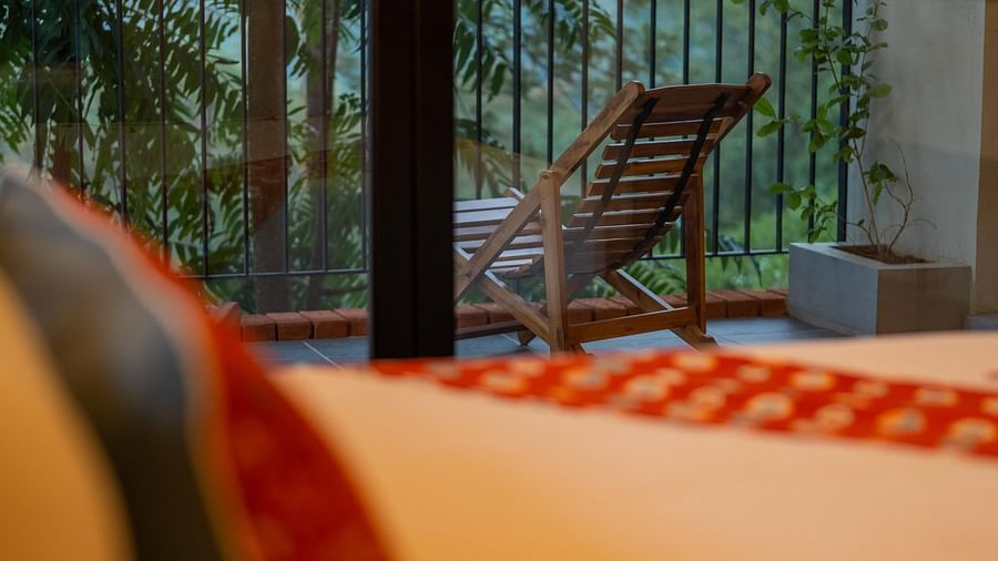  A comfortable bed with a decorative pillow, offering a view of a balcony with a lounge chair and lush greenery at Vaasta Vagamon.