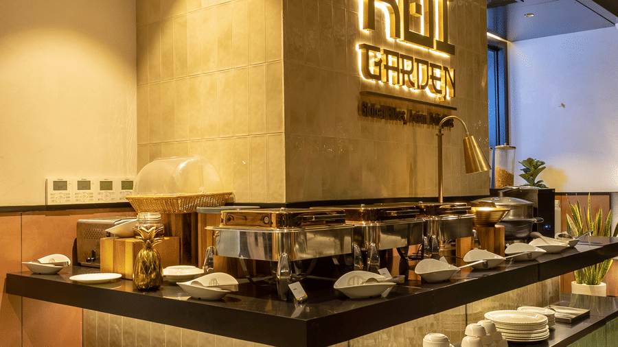 A buffet serving station inside Koi Garden. Covered dishes rest on the counter surface under lighting. The restaurant logo is fixed to the pillar structure above.