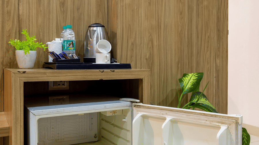 Deluxe Room featuring an open minibar with cold drinks and water bottles in it and tea and coffee maker set on the top at Hotel Corporate Suites