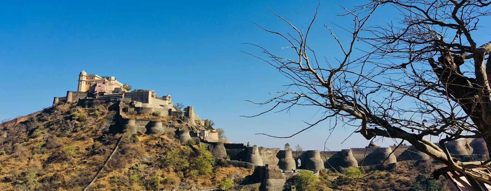 A historic fort situated on a rugged hilltop with stone walls extending along the terrain, under a clear blue sky.