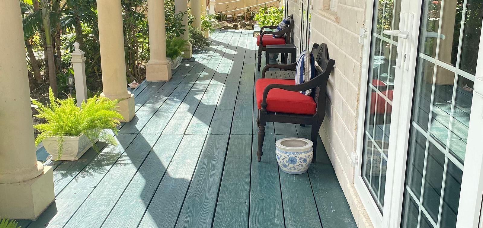 Outdoor walkway with green wooden flooring and red chairs outside a room | A Stone's Throw Away