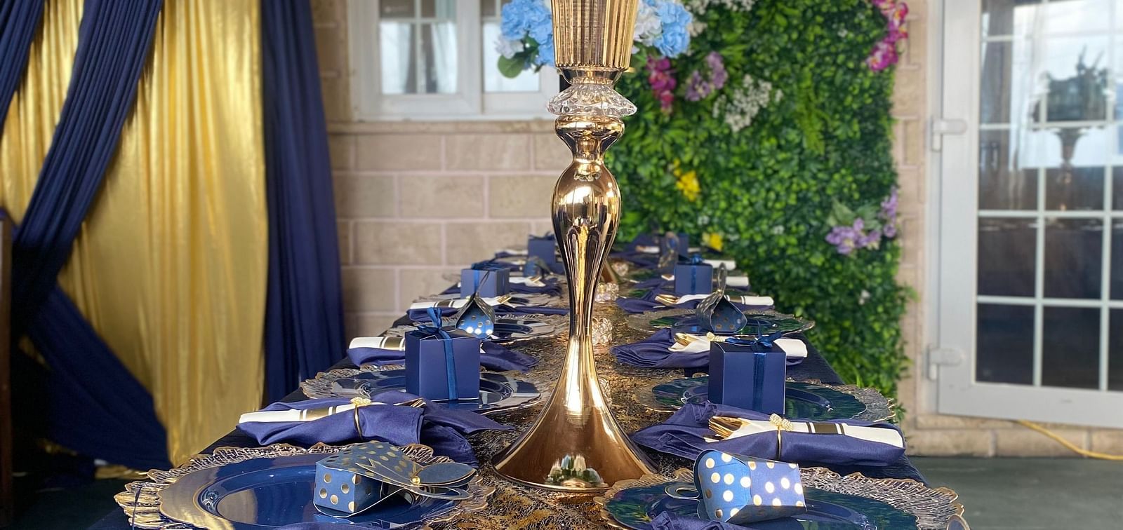 Long banquet table with navy blue napkins, golden cutlery, and tall floral centerpiece | A Stone's Throw Away