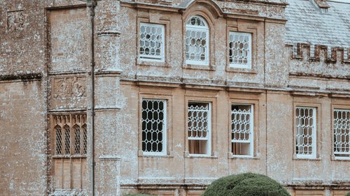 An old mansion with stone covering the outside walls and a garden in the foreground