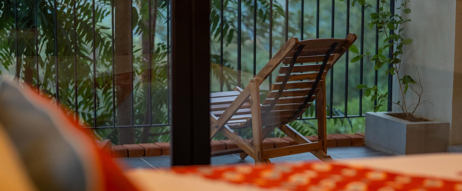 A comfortable bed with a decorative pillow, offering a view of a balcony with a lounge chair and lush greenery at Vaasta Vagamon.