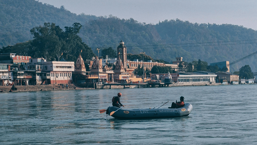 People on a boat, rafting on a calm river with mountains in the backdrop.