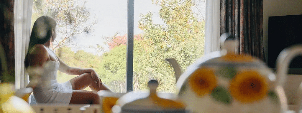 A woman sitting near a sunlit window with a floral teapot and teacups on the table in the foreground at Karma Chalets.