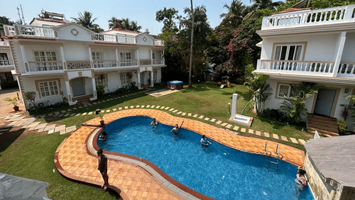 The swimming pool next to accommodation buildings and trees in between them at Richmonde Ananta Elite, Goa