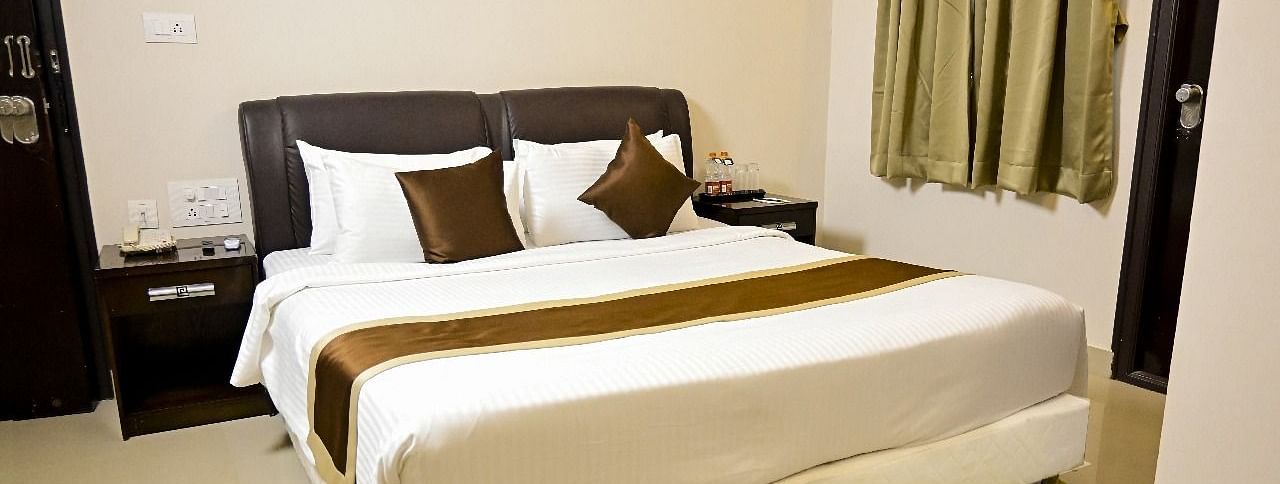  A comfortable hotel room at TGI Livancia Hillside, JC Nagar, Mysore, with a neatly made double bed, bedside tables with lamps, and curtains on the window.