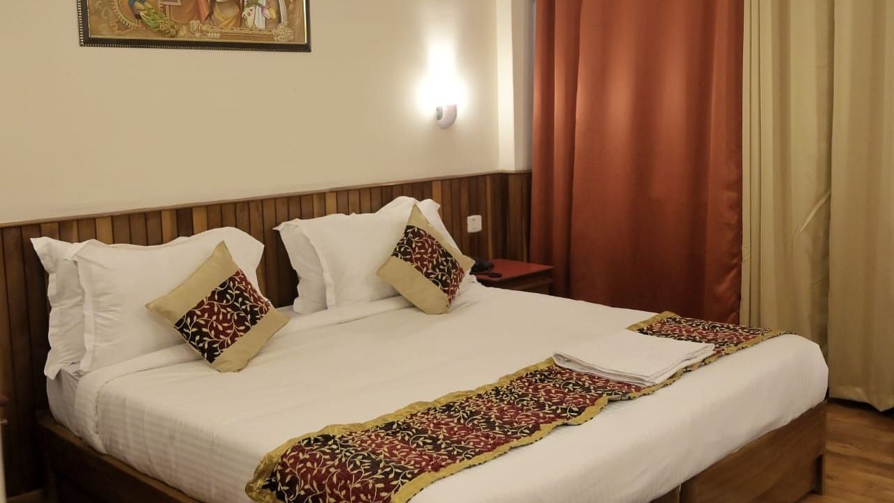 An image of the super deluxe room at Ecotel Chiminda, Pelling featuring a queen size bed, bed side table, decorative lighting, and a painting hung on the wall