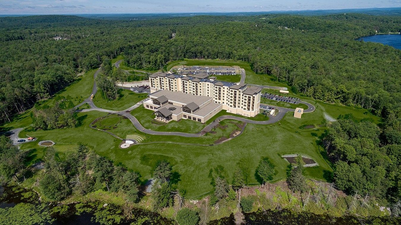 aerial view of YO1 Longevity and Health Resorts amidst vast green lawns and dense forests, with winding pathways and a large body of water in the distance. 