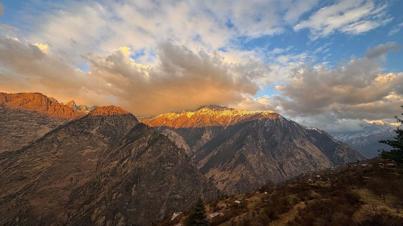 Mountain range at sunset with clouds above, rugged slopes, and warm light casting shadows on the landscape.