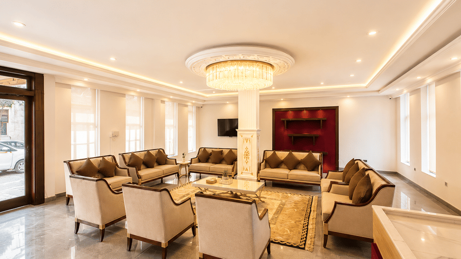 Hotel lounge with brown sofas and armchairs set around a round table, a large pendant light overhead and polished marble flooring below.
