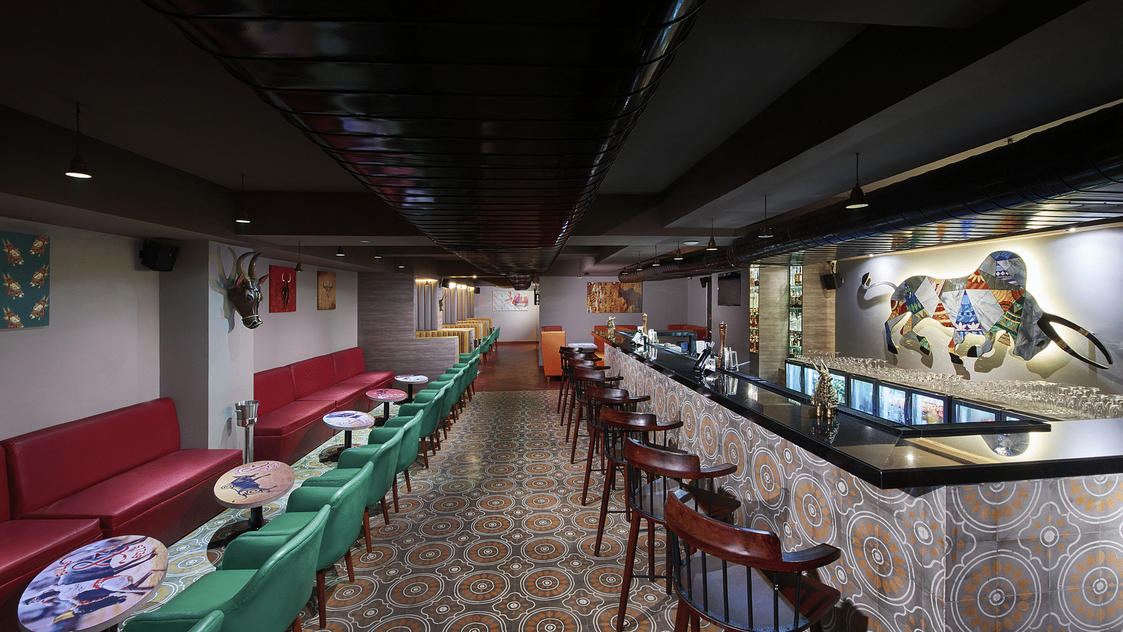 A brightly lit bar with red couches, a long bar counter, and a colorful wall mural | Regency Tirunelveli By GRT Hotels