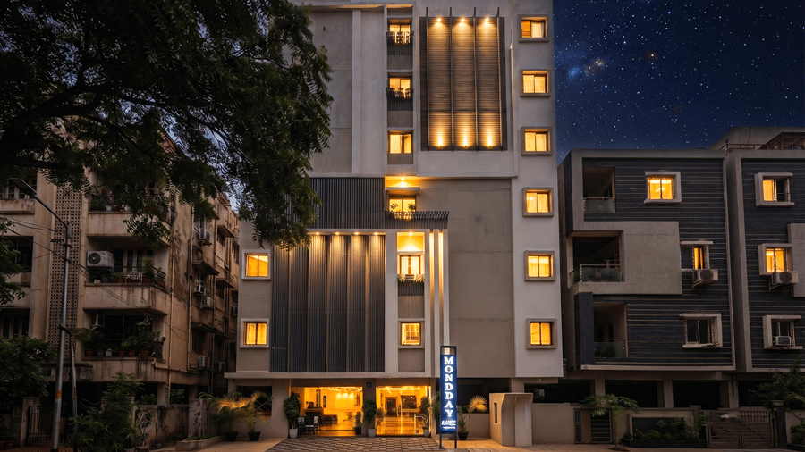Front facade of Monday Hotels & Suites Madhapur, Hyderabad lit at night under a starry sky, with warm window lights, a blue vertical sign and a lit entrance.
