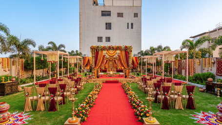 Outdoor wedding mandap setup at Lords Inn Sangam, Bhopal with a decorated stage, red carpet aisle, floral arrangements, and seating on the lush green lawn.