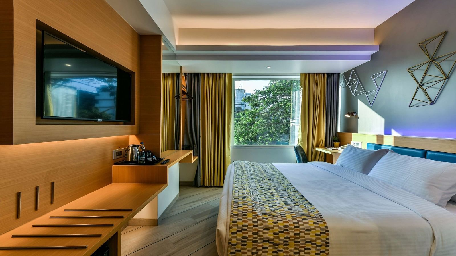A spacious room featuring a large bed and a window with curtains pulled to the side, offering a view of trees, at Indie Stays, BKC Kalina.