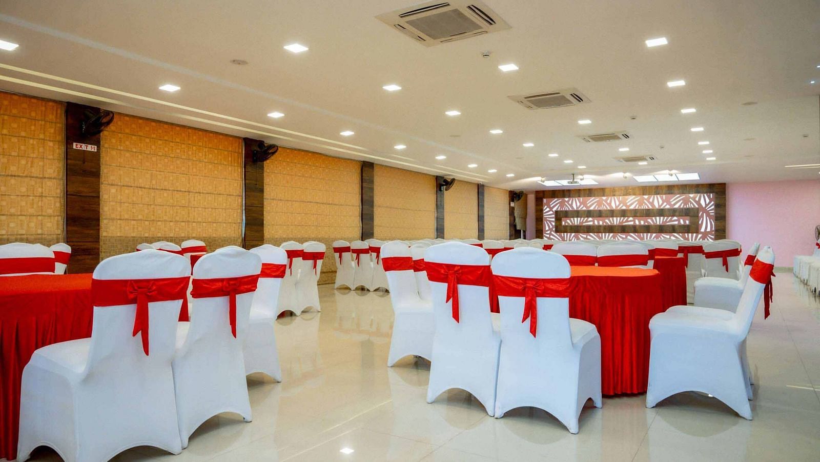 A large event space at Mansha Hotel Regency with numerous round tables covered in red tablecloths and white chairs.