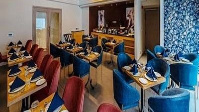 A side view of a restaurant seating area with chairs and tables set for diners with lights from the ceiling at Hotel Saket 27, New Delhi