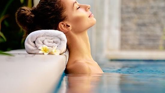 A person in the pool resting their neck on the deck with a towel
