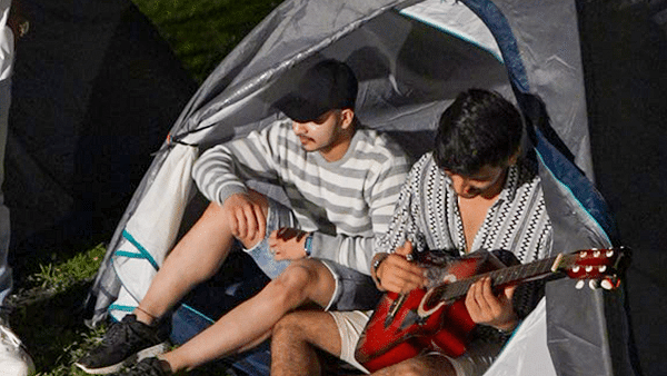Two men sitting in a tent playing guitar at night during a camping trip | Diamond Parks, Pune.