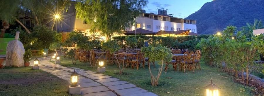 An outdoor scene at dusk where a pathway leads toward a building, which is illuminated with warm lights - Bamboo Saa Resort & Spa, Udaipur