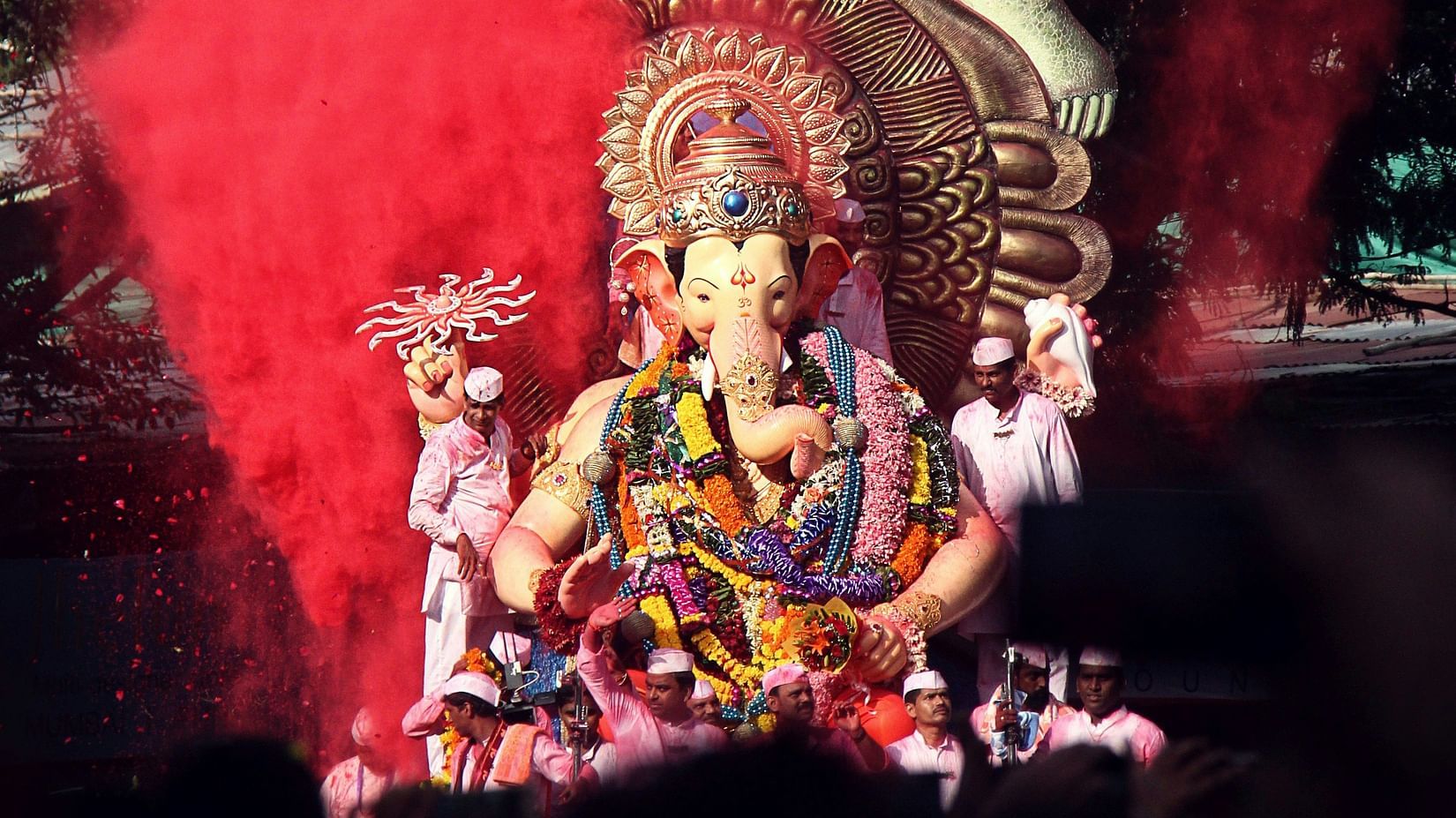 a ganesha's idol kept on a chariot while going for a visarjan with colours being thrown on it