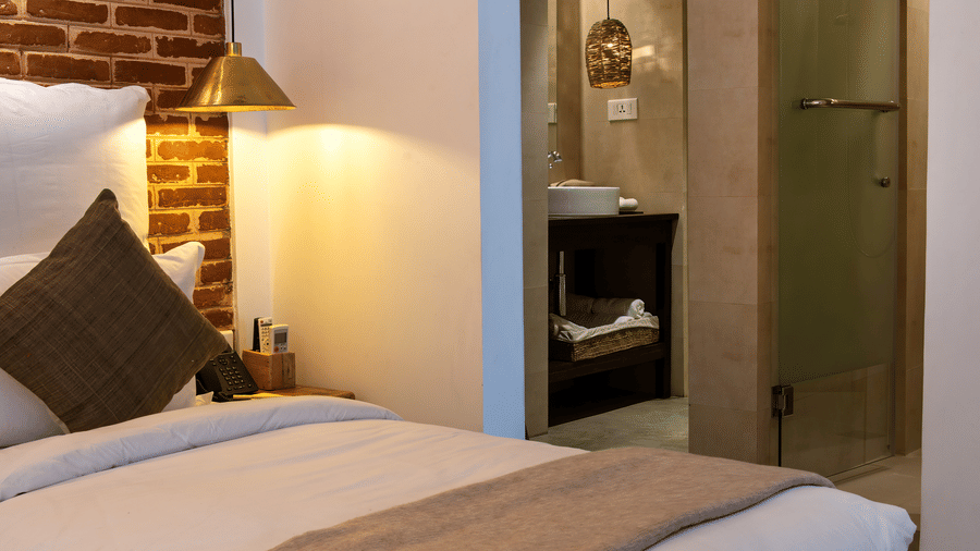 Room with twin bed, bed side table, lamp, and the washroom area - The Nanee