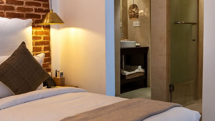 Room with twin bed, bed side table, lamp, and the washroom area - The Nanee