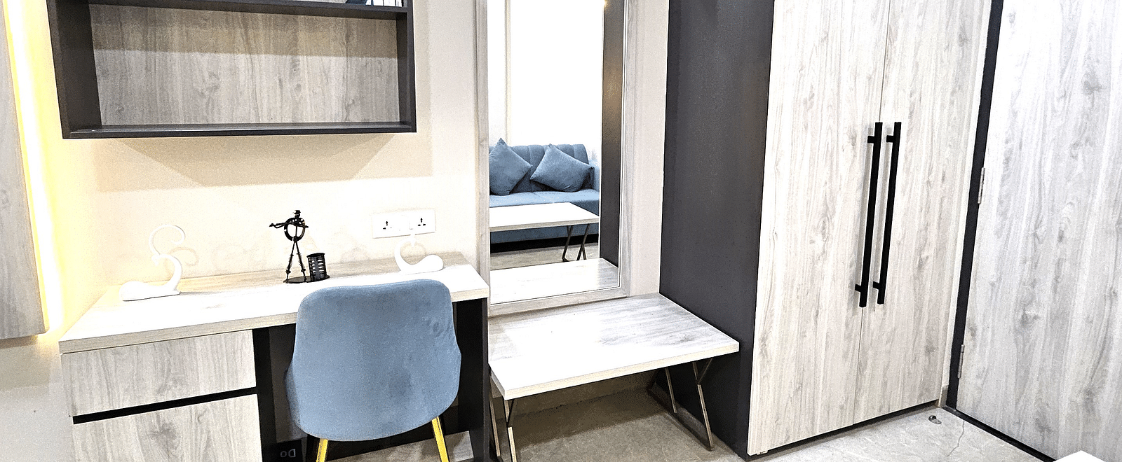 Modern workspace in a studio room featuring a sleek desk with storage, a comfortable upholstered chair, open shelves, a full-length mirror with a bench, and a spacious wardrobe for added convenience - Urban Suites by BluSalzz, Jaipur